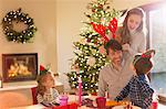 Family wearing elf and costume reindeer antlers at Christmas dining table