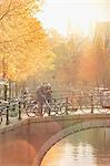 Young couple with bicycles taking selfie with selfie stick on bridge over canal in Amsterdam