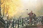 Young couple with bicycles taking selfie with selfie stick on autumn bridge, Amsterdam