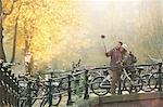 Young couple with bicycles taking selfie with selfie stick on autumn bridge, Amsterdam