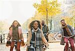 Smiling young friends bike riding on urban autumn street