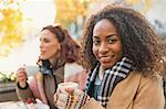 Portrait smiling young woman in warm clothing drinking espresso at sidewalk cafe