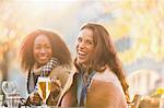 Portrait laughing young women friends drinking beer at autumn sidewalk cafe