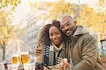 Portrait smiling young couple hugging and drinking beer at autumn sidewalk cafe
