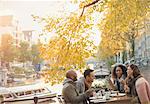 Friends laughing and eating cheesecake dessert at autumn sidewalk cafe along canal, Amsterdam