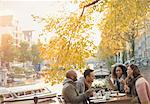 Friends laughing and eating cheesecake dessert at autumn sidewalk cafe along canal, Amsterdam