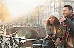 Young couple with bicycles on urban bridge over canal, Amsterdam