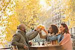 Smiling friends toasting beer glasses at autumn sidewalk cafe