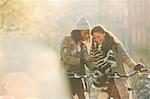 Young women friends with bicycles looking at cell phone on sunny autumn street