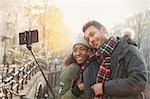 Affectionate couple hugging and taking selfie with selfie stick on autumn bridge, Amsterdam