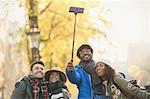 Smiling young couple friends taking selfie with selfie stick on autumn street