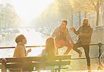 Young friends talking, hanging out on sunny urban autumn bridge over canal, Amsterdam