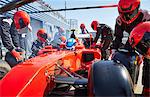 Pit crew replacing tires on formula one race car in pit lane