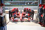 Pit crew pushing formula one race car into repair garage