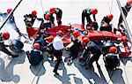 Manager with stopwatch timing pit crew replacing tires on formula one race car in pit lane