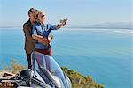 Senior couple taking selfie next to motorcycle overlooking sunny ocean view