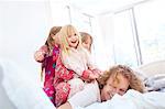 Playful daughters laying on top of father on bed