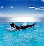 A man in a suit on a lilo in a swimming pool, a laptop on his lap.