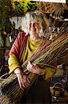 Smiling woman holding a willow bundle in a basket weaver's workshop.