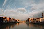 The Ponte Vecchio and Arno River in Florence, under a cloudy sky at dusk. Flat calm water.