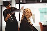 Female hairdresser styling clients hair in saloon