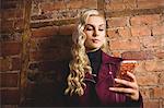 Beautiful blonde woman standing against brick wall using mobile phone