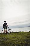 Athlete standing with his bicycle on grass near the sea
