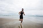Man in swimming costume and swimming cap running on beach