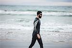Handsome athlete in wet suit walking on beach