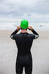 Rear view of athlete in wet suit wearing swim cap on the beach