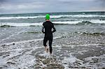 Rear view of athlete in wet suit running towards the sea