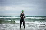 Athlete in wet suit standing with arms crossed in sea on beach