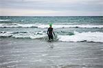 Rear view of athlete in wet suit walking towards the sea
