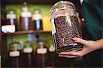 Mid section of female shopkeeper holding jar of coffee beans at counter in shop