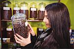 Beautiful woman holding jar of coffee beans at counter in shop