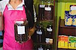 Mid section of female shopkeeper holding jar of coffee beans at counter in shop