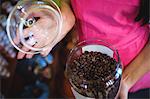 Close-up of female shopkeeper holding jar of coffee beans at counter in shop