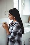 Thoughtful woman holding cup tea in kitchen at home