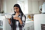 Woman using mobile phone while having breakfast in kitchen at home