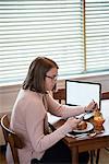 Woman using mobile phone while having breakfast in living room at home