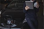 Man using digital tablet while charging electric car in garage