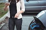 Mid section of woman using mobile phone while charging electric car on street