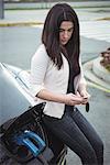 Beautiful woman using mobile pone while charging electric car on street car