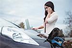 Beautiful woman talking on mobile phone while charging electric car on street