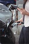 Mid section of woman using digital tablet while charging electric car at vehicle charging station