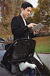 Man using digital tablet while charging electric car at electric vehicle charging station