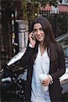 Woman talking on mobile phone while car being charged in background at electric vehicle charging station