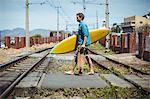 Man carrying skateboard and surfboard crossing railway track