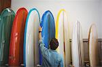 Rear view of man looking at colorful surfboards in shop