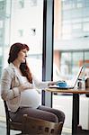 Pregnant businesswoman using laptop in office cafeteria